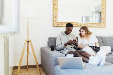 Young man using smart phone sitting by girlfriend in living room at home - MEUF05327