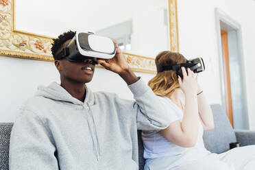 Young couple wearing virtual reality simulators sitting on sofa at home - MEUF05331