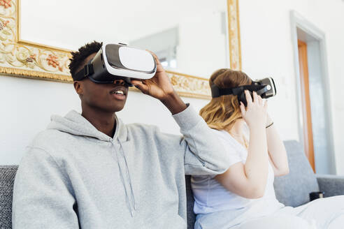 Junges Paar mit Virtual-Reality-Simulatoren sitzt zu Hause auf dem Sofa - MEUF05331