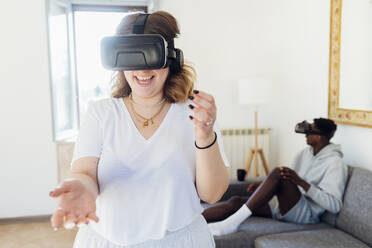 Fröhliche Frau, die einen Virtual-Reality-Simulator trägt und sich zu Hause amüsiert - MEUF05334