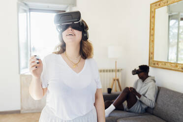 Glückliche Frau mit Virtual-Reality-Simulator im Wohnzimmer - MEUF05335