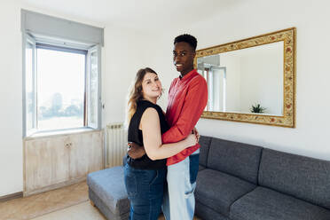 Glückliches Paar umarmt sich im Wohnzimmer zu Hause - MEUF05336