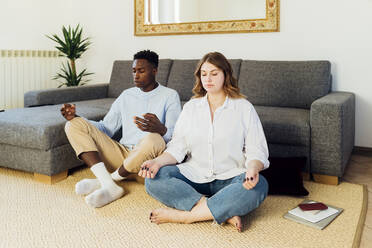 Young couple meditating sitting on carpet in living room at home - MEUF05351