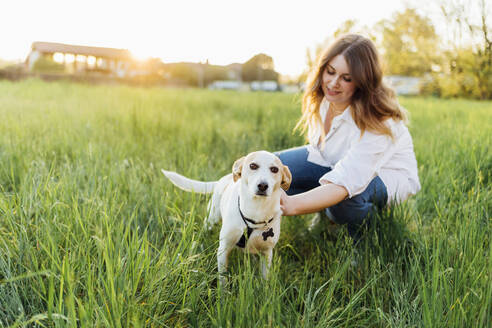 Lächelnde junge Frau mit Hund in der Natur - MEUF05375