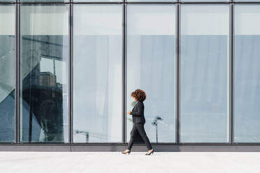 Businesswoman holding bag walking by glass wall - MEUF05405