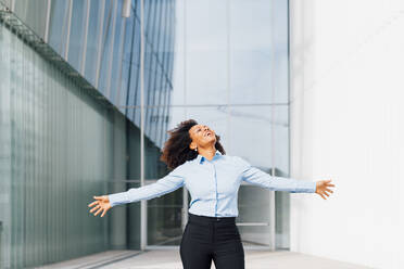 Happy businesswoman with arms outstretched standing in front of office building - MEUF05413