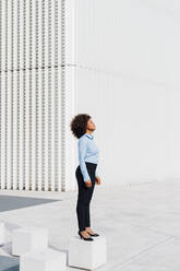Afro businesswoman standing on concrete block - MEUF05418