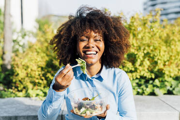 Glückliche Geschäftsfrau isst Salat an einem sonnigen Tag - MEUF05438