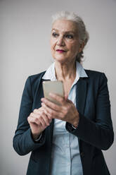Geschäftsfrau mit Smartphone stehend vor weißem Hintergrund - JOSEF08885