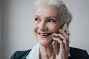 Glückliche ältere Geschäftsfrau, die mit einem Mobiltelefon vor weißem Hintergrund spricht - JOSEF08889