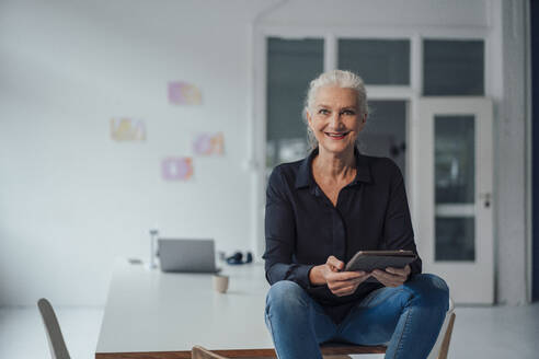 Lächelnde ältere Geschäftsfrau mit Tablet-PC auf dem Schreibtisch im Büro - JOSEF08893