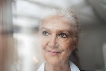Smiling senior businesswoman with gray hair looking through window - JOSEF08905