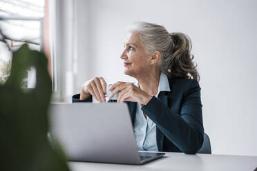 Businesswoman with coffee cup sitting at desk in office - JOSEF08920