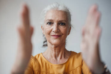 Senior woman with gray hair gesturing with hand against white background - JOSEF08970