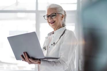 Happy doctor wearing eyeglasses using laptop - JOSEF08979