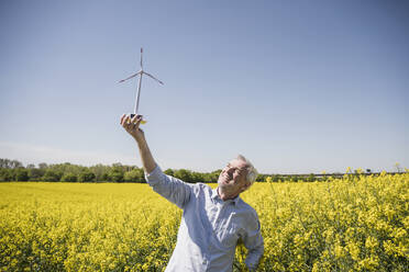 Lächelnder Mann betrachtet das Modell einer Windkraftanlage auf einem Feld - UUF25872