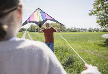 Glücklicher Großvater unterrichtet Enkelin beim Drachensteigenlassen auf einem Feld - UUF25893