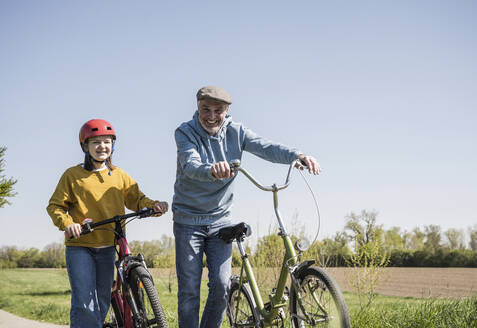 Glücklicher Großvater und Enkelin gehen mit dem Fahrrad an einem sonnigen Tag spazieren - UUF25900