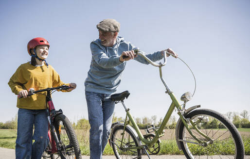 Lächelnder Großvater und Enkelin mit Fahrrad an einem sonnigen Tag - UUF25901
