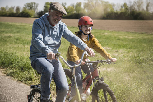 Lächelnder Großvater mit Enkelin beim Radfahren an einem sonnigen Tag - UUF25902