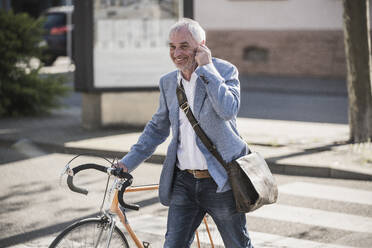 Glücklicher Geschäftsmann mit Fahrrad an einem sonnigen Tag - UUF25906