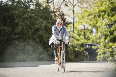 Businessman listening music through wireless headphones cycling on road - UUF25909