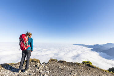 Deutschland, Bayern, Wanderin steht auf einem Berggipfel und bewundert die nebelumhüllten Gipfel der Bayerischen Voralpen - FOF13152
