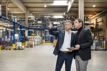 Businessman discussing with colleague holding tablet PC in factory - PESF03651