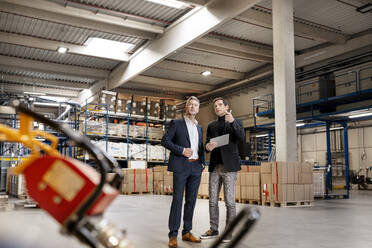 Mature businessman discussing with colleague holding tablet PC in factory - PESF03655