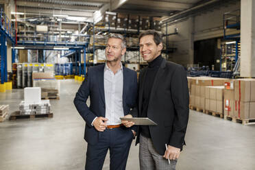 Confident businessman with colleague holding tablet PC in warehouse - PESF03658