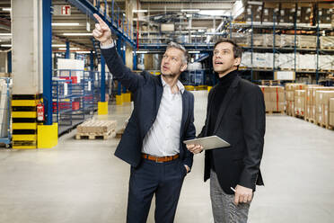 Mature businessman pointing and discussing with colleague in meeting at warehouse - PESF03660