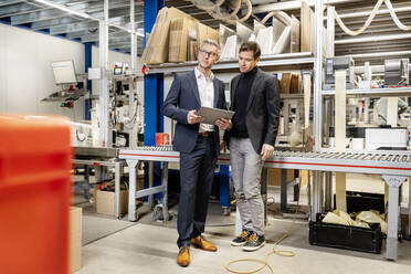 Businessman holding tablet computer discussing with colleague in factory - PESF03663