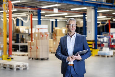 Confident businessman with tablet PC standing in factory - PESF03664