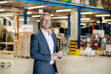 Smiling businessman with tablet PC standing at warehouse - PESF03665