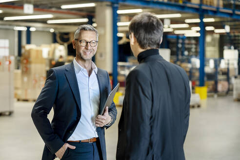 Älterer Geschäftsmann mit Hand in der Tasche diskutiert mit einem Kollegen in einer Fabrik - PESF03666