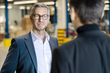 Confident businessman discussing with colleague in warehouse - PESF03667