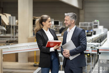 Happy businesswoman discussing with businessman in warehouse - PESF03678