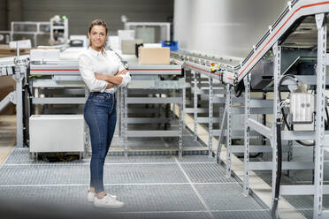 Smiling businesswoman with arms crossed standing in warehouse - PESF03692