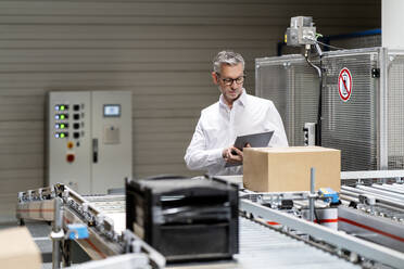 Businessman using tablet computer by conveyor belt in warehouse - PESF03701