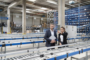 Young businesswoman discussing with colleague by conveyor belt in factory - PESF03702