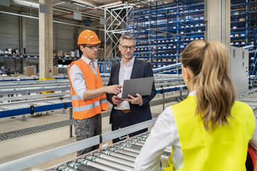 Älterer Manager diskutiert mit einem Kollegen über einen Laptop in einer Fabrik - PESF03711