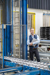 Mature businessman with laptop standing at factory - PESF03732