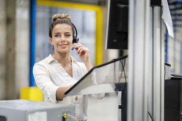 Lächelnde Geschäftsfrau mit Headset in einer Fabrik - PESF03745