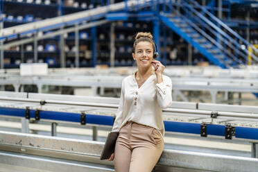 Smiling businesswoman talking on headset in factory - PESF03749