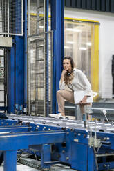 Junge Geschäftsfrau mit Bein auf Förderband in Fabrik - PESF03756