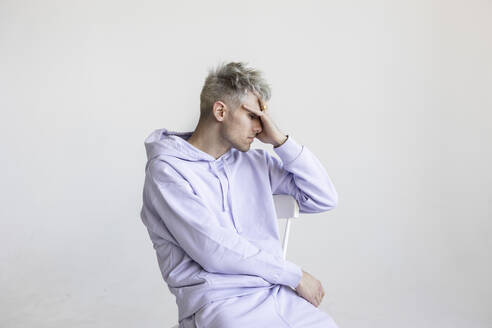 Stressed man sitting on chair against white background - LHPF01418