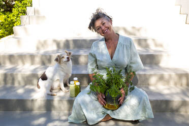 Glückliche Frau mit Pflanze neben Hund auf Stufen sitzend - ESTF00036
