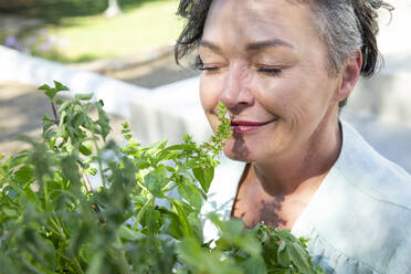 Lächelnde reife Frau riecht an Pflanzen an einem sonnigen Tag - ESTF00039