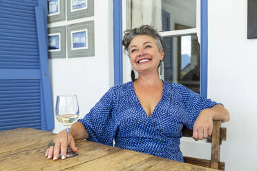 Glückliche reife Frau mit einem Glas Wein am Tisch sitzend - ESTF00061