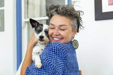 Glückliche reife Frau mit kurzen Haaren umarmt Hund zu Hause - ESTF00065